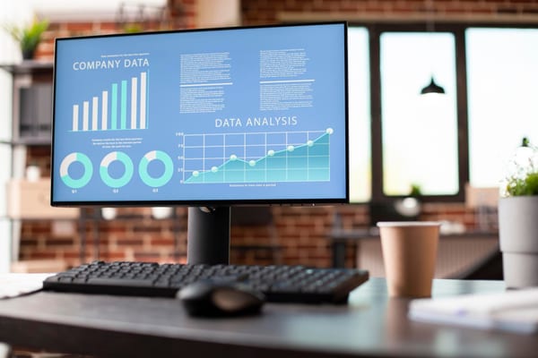 Pantalla de monitor en oficina luminosa con luz natural mostrando dashboard de análisis de datos con curva de crecimiento ascendente pronunciada, ilustrando el aumento exponencial del coste de IA al pasar de piloto a producción