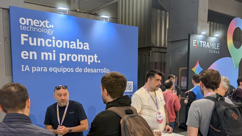 Stand de onext en La Nave con la lona «Funcionaba en mi prompt. IA para equipos de desarrollo» y varias personas conversando